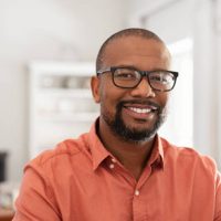 Smiling mature man wearing spectacles looking at camera. Portrait of black confident man at home. Successful entrepreneur feeling satisfied.